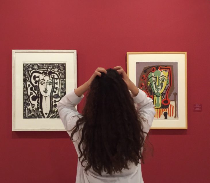 Chica con cabello largo y rizado mira pinturas en un museo con una pared roja