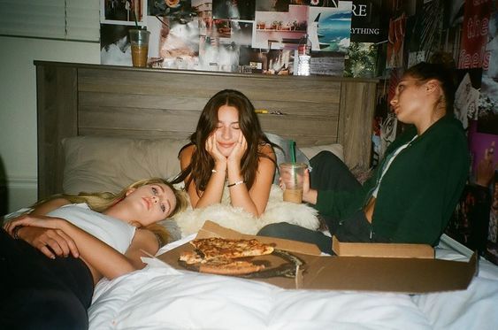 Tres amigos están acostados en la cama y comiendo pizza.