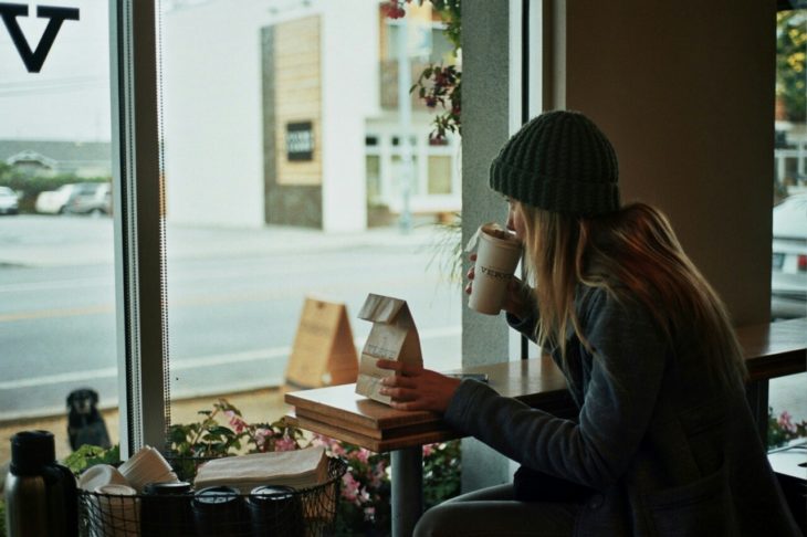 Chica rubia bebe café en la ventana de una cafetería