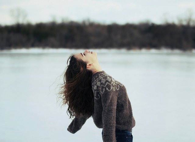 Mujer de cabello largo extiende sus brazos en la nieve.