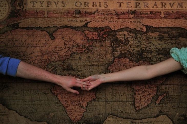 Una pareja abre los brazos y se toma de la mano en un mapa del mundo