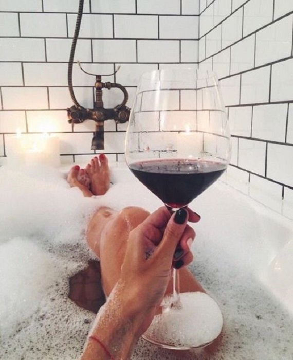 Chica bañándose en la bañera y bebiendo una copa de vino