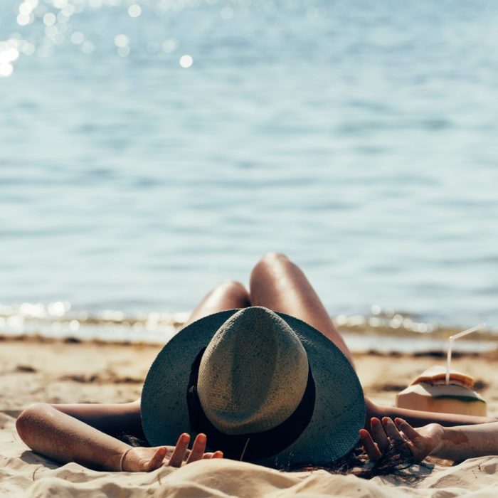 Mujer relajada en la playa con un sombrero para el sol y bebiendo agua de coco
