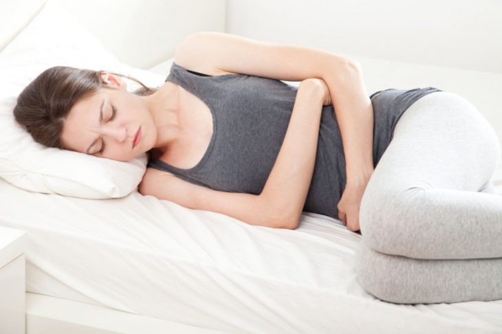 Mujer acostada y tocándose el estómago como señal de dolor