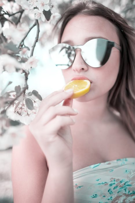 Chica con gafas de espejo comiendo limón