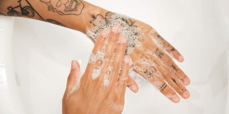 Imagen muestra manos tatuadas frotándose con jabón