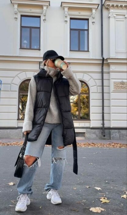 chica con jeans rotos, un chaleco oversized tomando café en una calle de la ciudad