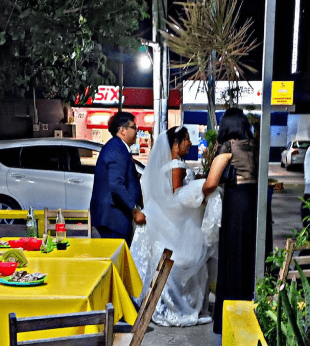 recién casados caminando por la calle al lado de una taquería, vestidos con sus trajes de boda