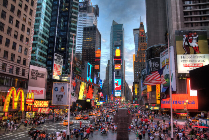 Imagen de Nueva York al anochecer, iluminada y con rascacielos visibles, y un gran flujo de gente caminando