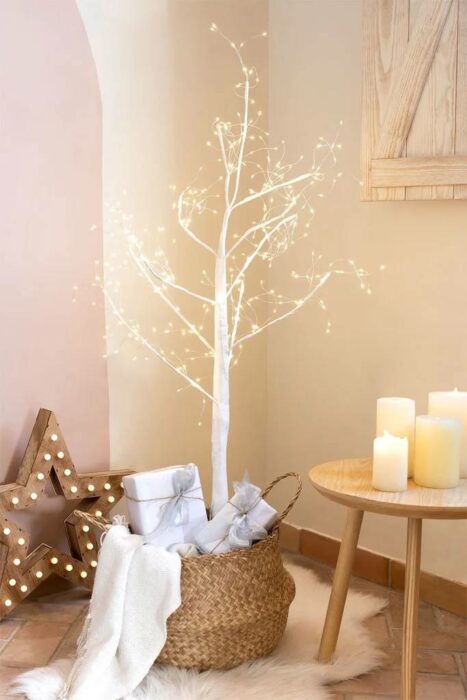 árbol de navidad con una rama seca en color blanco decorado con luces y velas al costado