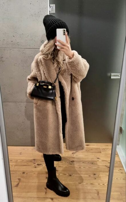 Foto de una chica en el espejo con gabardina furry y un gorro negro