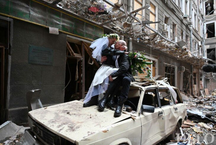 Pareja de novios sentados sobre un carro destrozado en medio de las ruinas de un edificio en Ucrania