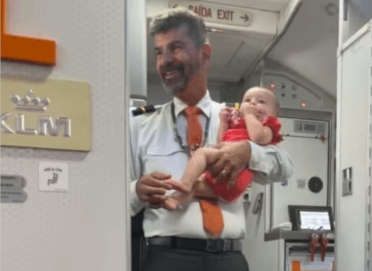 un sobrecargo sostiene a una bebé en brazos mientras está de pie cerca de la puerta del avión
