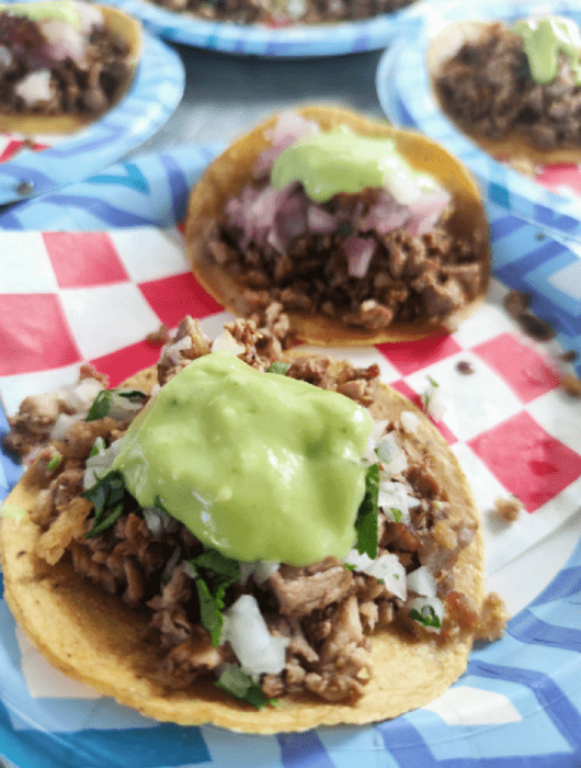 tacos de asada colocados en un plato con papeles de colores de base, acompañados de verduras y salsa verde