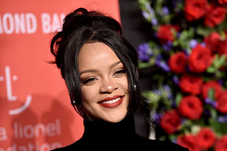 Rihanna sonriendo ligeramente en una alfombra roja con rosas
