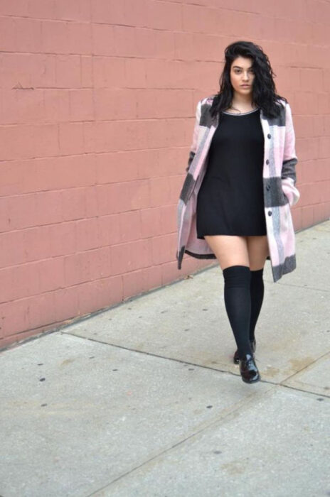 Mujer curvy luciendo un vestido negro con botas altas y camisa de cuadros en gris y rosa