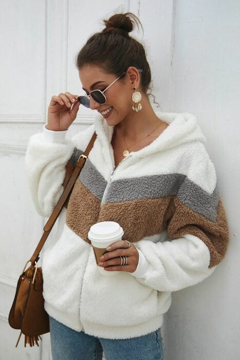 Chaqueta de cierre blanca con franjas café y gris, jeans y bolsa de mano color camel