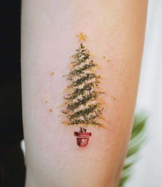Chica con un tatuaje de árbol navideño con estrella amarilla; Tatuajes para las chicas que aman Navidad