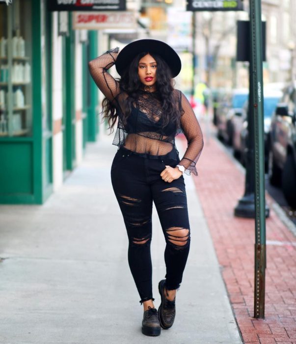 Chica curvy usando un pantalón de jean con rasgaduras y una blusa con transparencias en conjunto con un sombrero