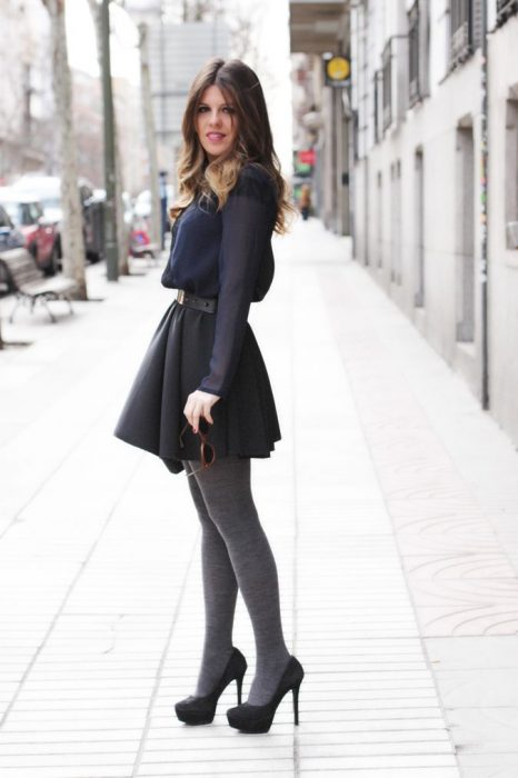 Chica usando un vestido corto de color gris con medias y tacones