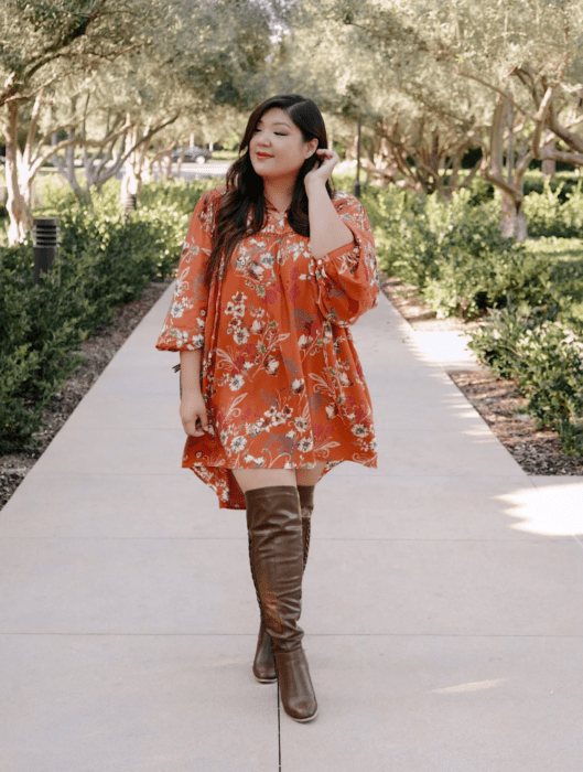 Chica usando outfit veraniego de vestido naranja con estampado, manga 3/4 y botas altas cafés