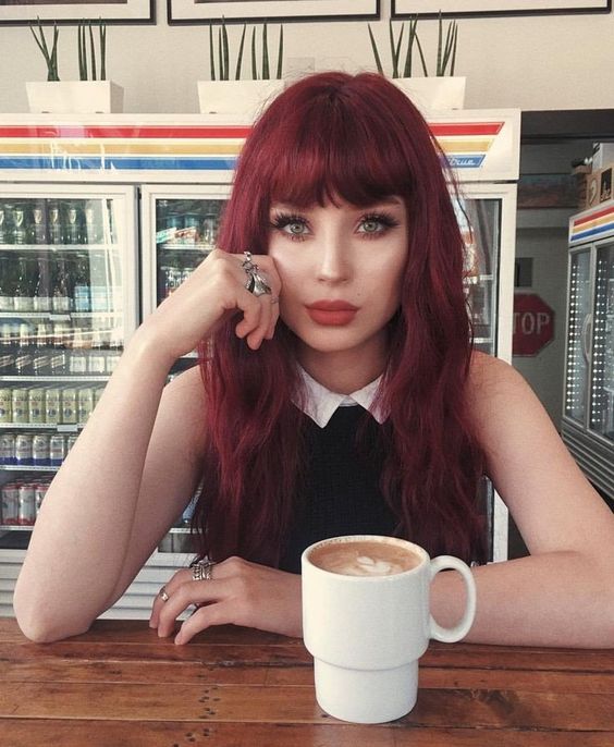 Chica sentada en una cafetería, bebiendo café, mostrando su cabello largo tono cherry wine
