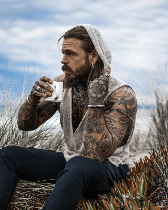 Hombre tatuado disfrutando de una taza de café mientras admira el paisaje