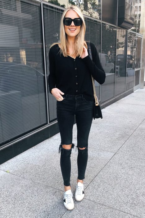Chica usando jeans rasgados, blusa de manga larga en color negro y tenis blancos, además de lentes oscuros y bolso negro