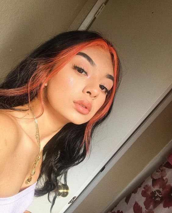 Chica morena clara de cabello largo y negro lleva mechones de cabello naranjas 
