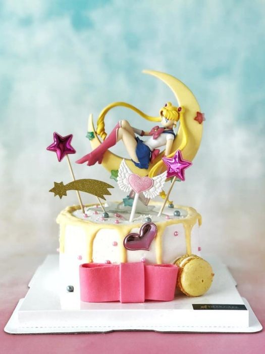 Pastel de Sailor Moon con base de fondant blanca, una figurilla de Serena sobre una luna y demás detalles