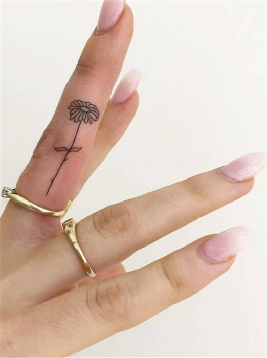 Chica con un tatuaje en forma de flor en el dedo medio