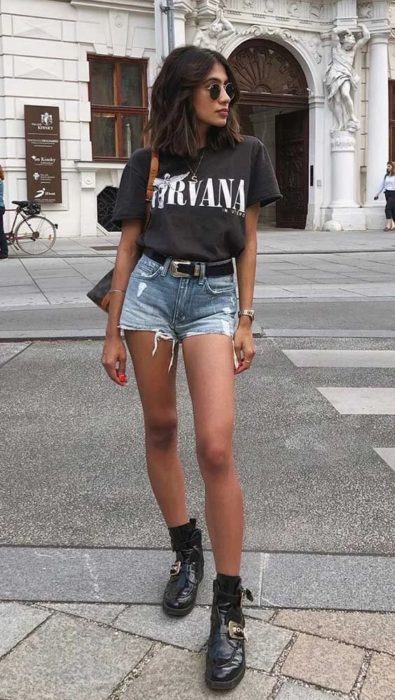 Chica con blusa de Nirvana negra y short de mezclilla con cinto y botas