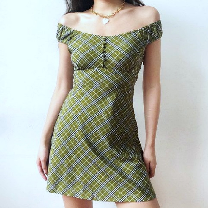 mujer con cabello largo vistiendo un vestido verde con estampado de cuadritos, caída a los hombros y botones en el escote