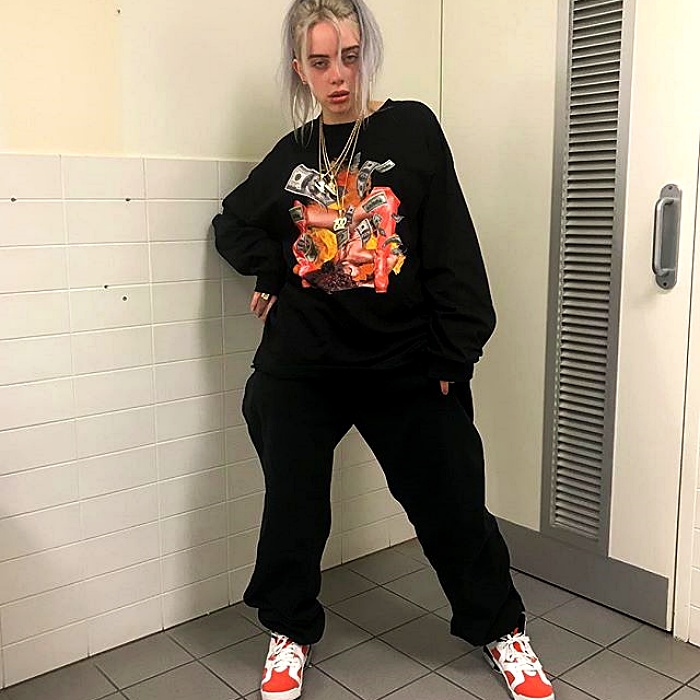 Billie Eilish con una sudadera negra, pants deportivos negros y tenis blancos con rojo