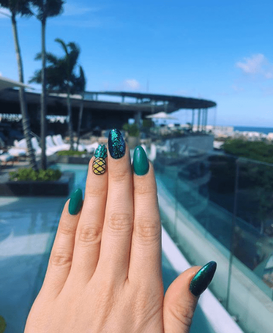 Manicura de uñas en tono verde con efecto cromado decorada con una piña amarilla