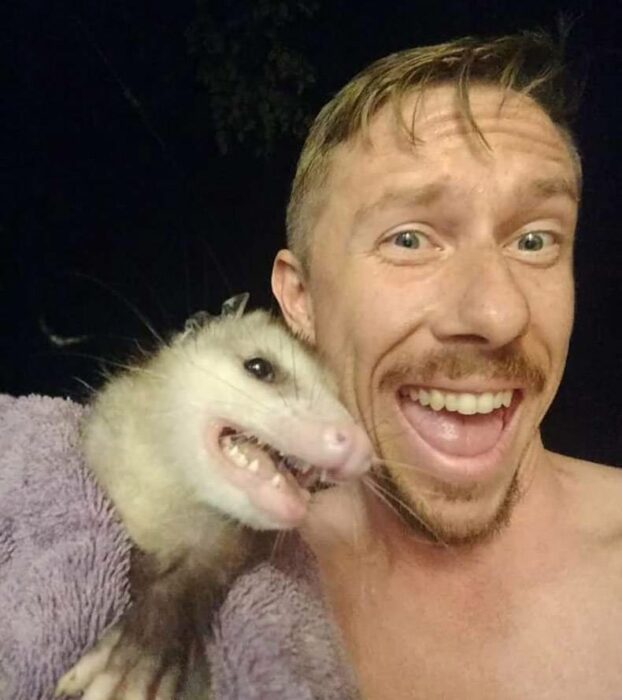 un hombre a lado de una zarigüeya sonriendo