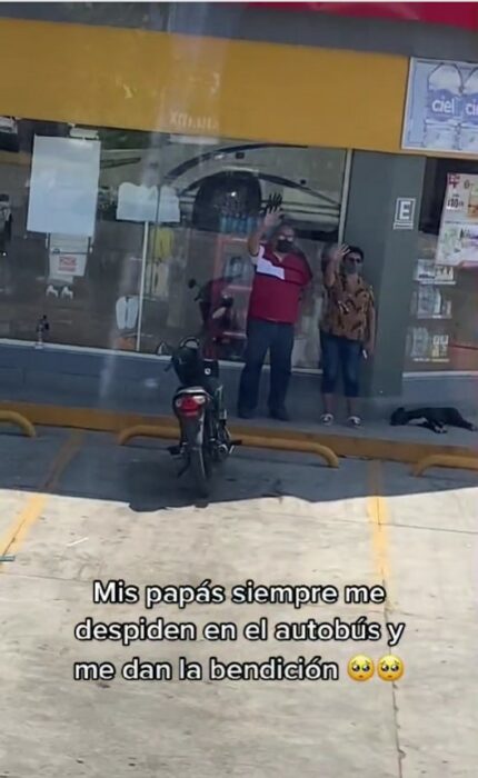 un hombre y una mujer parados frente a un Oxxo diciendo adiós con la mano