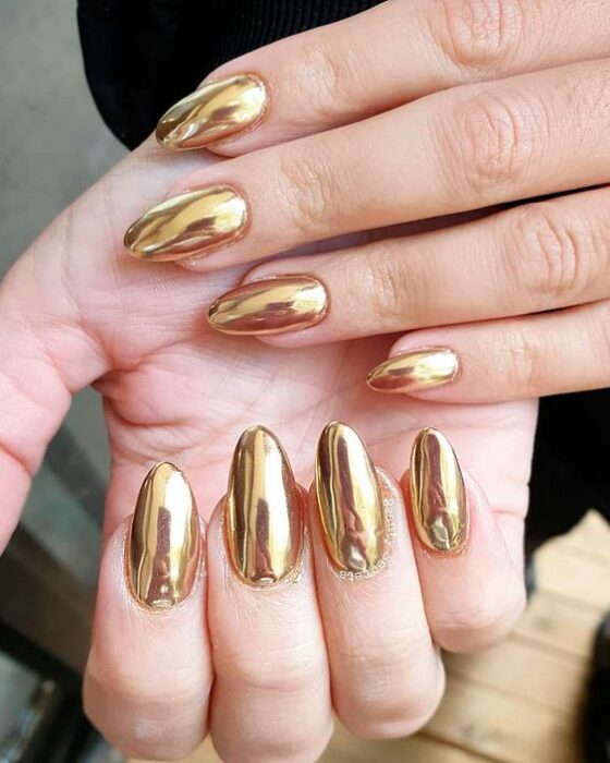 Chica usando unas uñas con tonos dorados brillantes