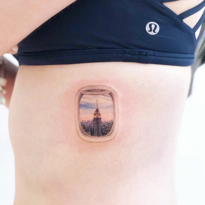 tatuaje de una vista a través de una ventana de avión en la costilla de una persona