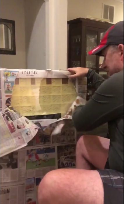 hombre sentado abriendo un cuadro envuelto con papel