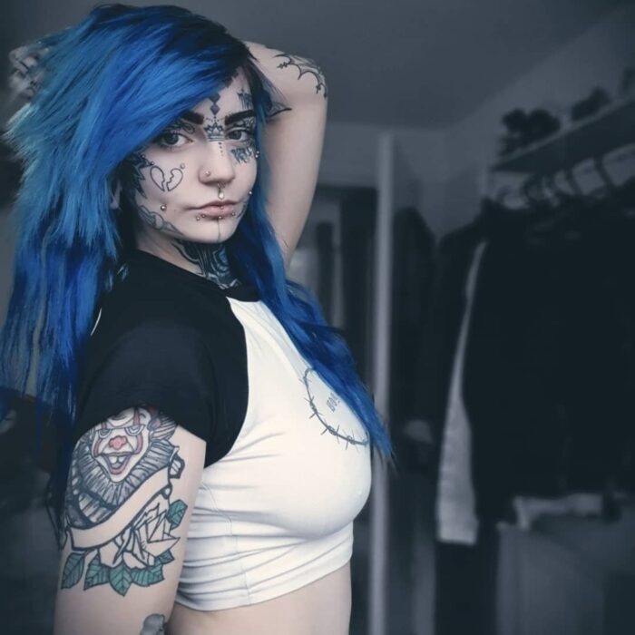 mujer de cabello azul con tatuajes en el rostro