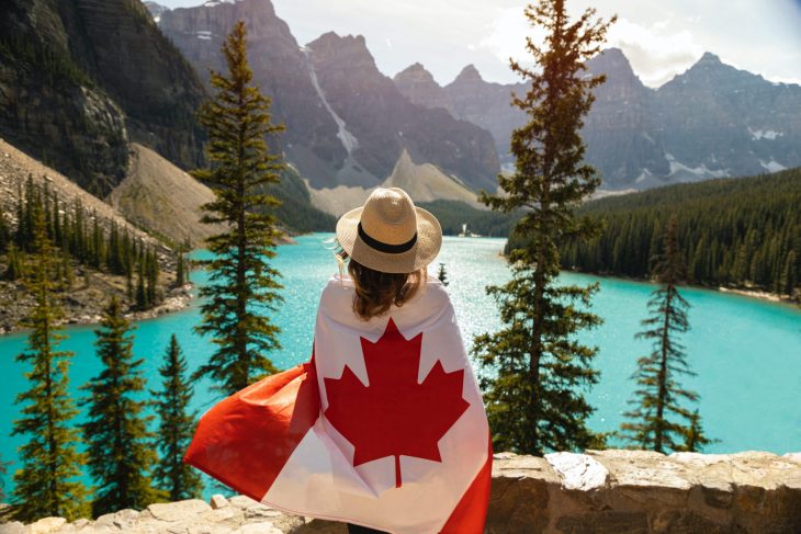 Chica abrazando una bandera de Canadá mientras mira un lago