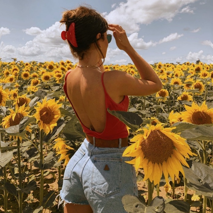 chica posando de manera original, con flores, en un campo abierto, frente a un espejo, con ropa trendy, jeans, falda, outfit lindo, botas, manicure, uñas postizas, lentes de sol