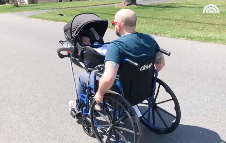 Hombre en silla de ruedas paseando a su bebé en un portabebé 