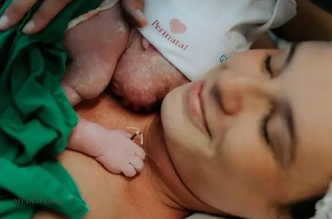 Mamá sosteniendo a su bebé en el pecho mientras él trae un Diu en la manita