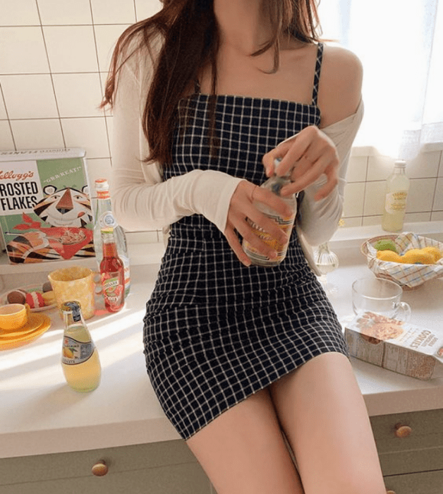 chica de cabello castaño usando un vestido negro ajustado de tirantes con cuadros blancos, cárdigan blanco de manga larga