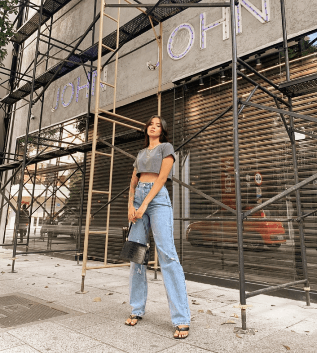 chica de cabello oscuro con crop top de manga corta, jeans holgados rotos, sandalias negras de tacón, bolso de mano negro
