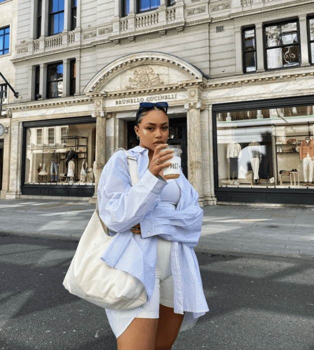 chica morena con lentes de sol, crop top beige de tirantes, shorts de ciclismo beige, camisa blanca de vestir oversized, bolso de cuero grande beige