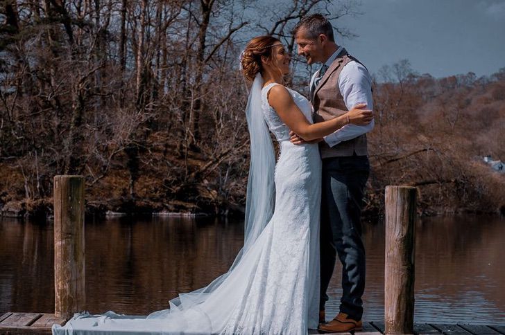 Pareja frente a un lago vestidos de novios mientras se casan 