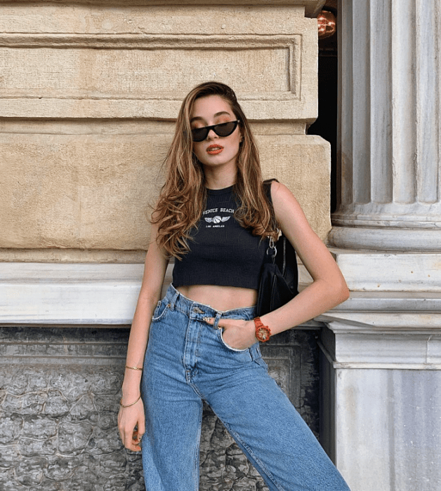 chica de cabello largo usando un crop top blanco, negro, beige, café, verde, azul de manga larga, corta, con jeans ajustados, pantalones negros de cuero, bolso pequeño de mano